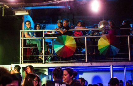Cabaretito Fusion Gay Bar in Mexico: People on a balcony, rainbow umbrellas, disco ball, and crowd below in a lively gay bar atmosphere.