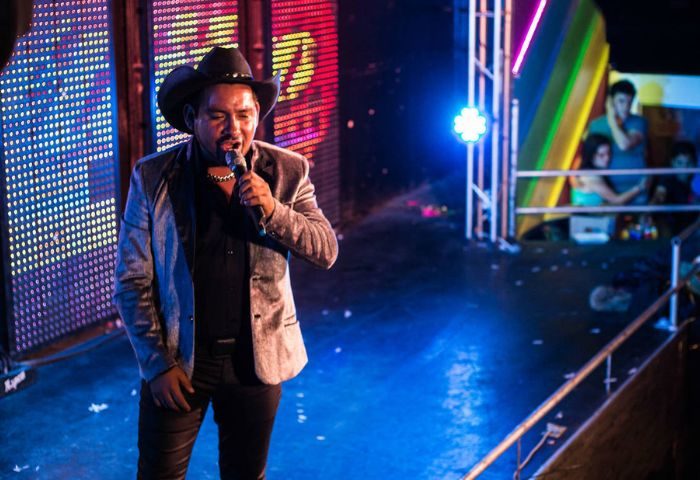 Singer at Cabaretito Fusion Gay Bar in Mexico. Man in cowboy hat performing on stage with colorful lights. Gay travel nightlife.