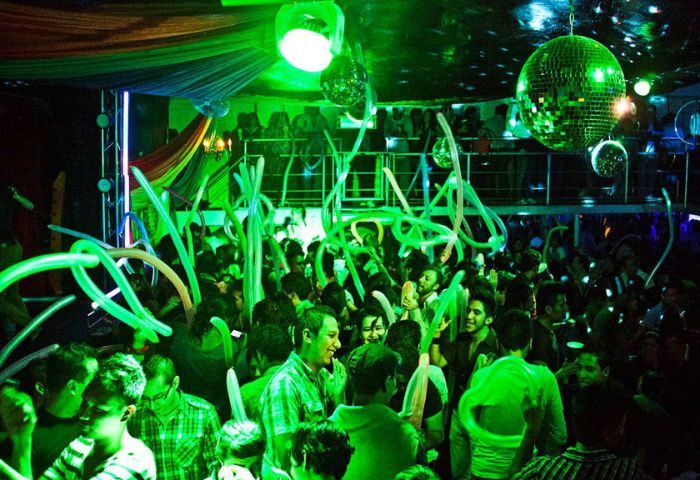 Crowded dance floor at Cabaretito Fusion, a gay bar in Mexico, with green lighting, disco balls, and festive balloons. Gay travel.