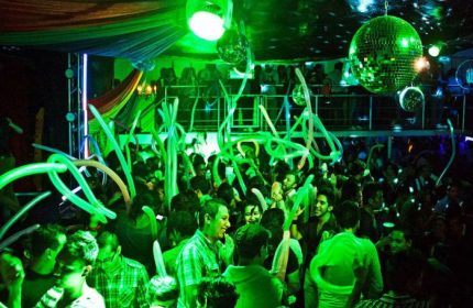 Crowded dance floor at Cabaretito Fusion, a gay bar in Mexico, with green lighting, disco balls, and festive balloons. Gay travel.