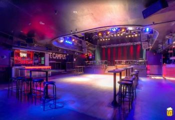 Interior of Campus, a gay strip bar in Montreal. Stage, bar, tables, and stools are visible. Blue and red lighting.