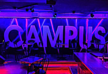Interior of Campus, a gay strip bar in Montreal. Blue and red neon lights illuminate the tables and bar area. Nightlife for gay men.