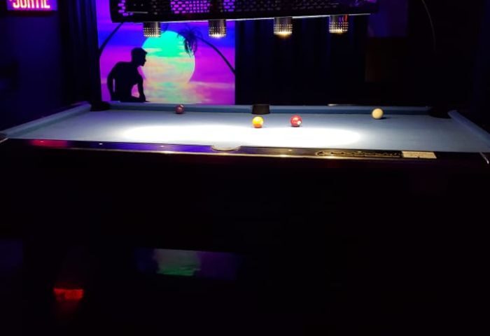 Pool table at Campus, a gay strip bar in Montreal. Neon lights, silhouette of a man, and a tropical scene in the background. Gay nightlife.