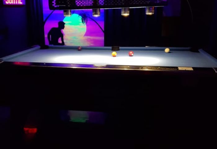 Pool table at Campus, a gay strip bar in Montreal. Neon lights, silhouette of a man, and a tropical scene in the background. Gay nightlife.
