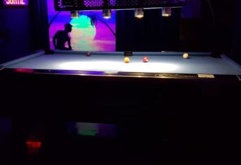 Pool table at Campus, a gay strip bar in Montreal. Neon lights, silhouette of a man, and a tropical scene in the background. Gay nightlife.