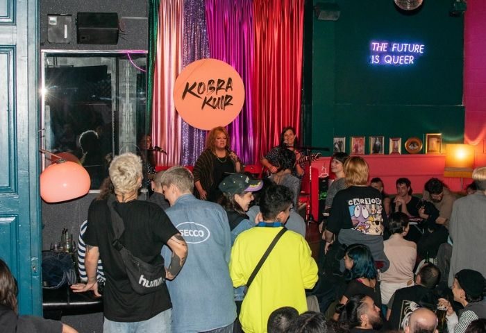 Candy Darling Gay Bar in Barcelona: Live music performance at a queer venue. The Future is Queer neon sign. Crowd enjoying the show.
