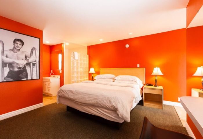 Canyon Club Hotel bedroom in Palm Springs. Gay accommodation with orange walls, bed, and a black and white photo of a man in swimwear.