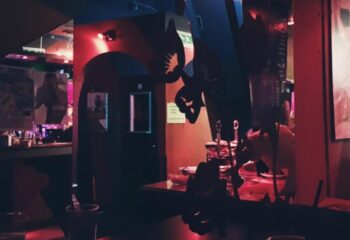 Interior shot of Censured Club Rome, a gay bar. Red lighting, bar area, decorations, and a glimpse of patrons create a vibrant atmosphere.