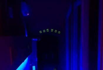 Inside Censured Club Rome, a gay club. Dark interior with blue lighting. Neon green symbols above an archway. Gay men travel.