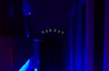 Inside Censured Club Rome, a gay club. Dark interior with blue lighting. Neon green symbols above an archway. Gay men travel.