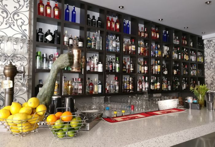 Central Bar Books, a gay bar in Sitges, Spain. Shelves stocked with liquor bottles, fruit, and a unique arm sculpture behind the bar.