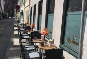 Centralhjornet Copenhagen outdoor seating. Gay bar with rainbow flags on windows. Tables with lamps. Gay travel advice.