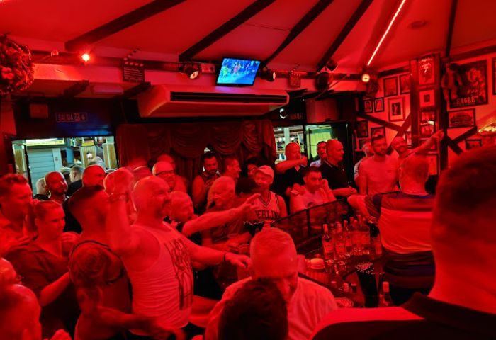 Centre Stage Bar, Gran Canaria. Red-lit interior of a gay bar, crowded with men. TV screen above the bar. Nightlife scene.