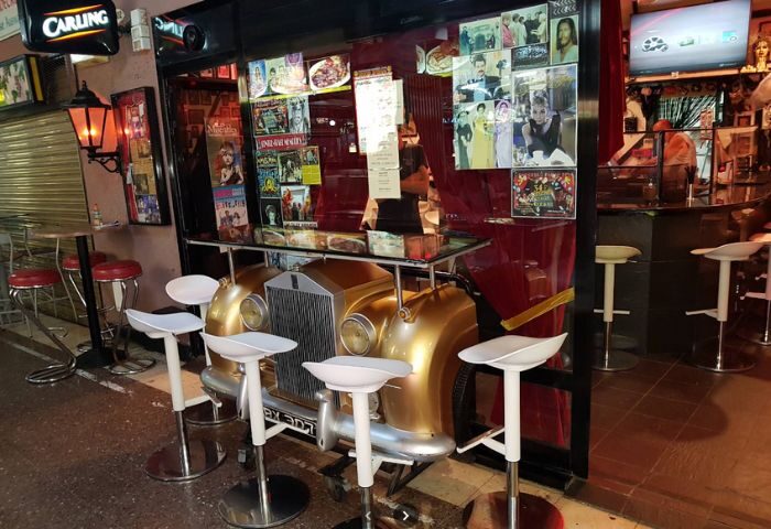 Centre Stage Bar, a gay bar in Gran Canaria. Car-themed bar with stools, posters, and a Carling sign. Gay travel destination.