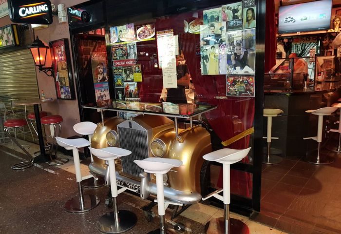Centre Stage Bar, a gay bar in Gran Canaria. Car-themed bar with stools, posters, and a Carling sign. Gay travel destination.