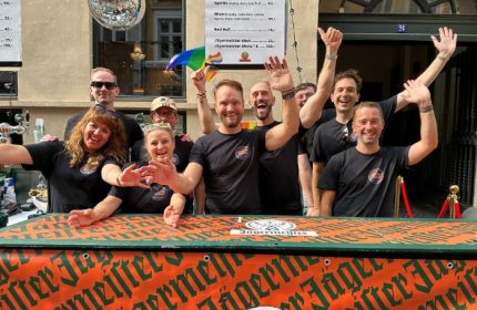 Centre Stage CPH: Gay bar staff in Copenhagen waving. Disco ball, rainbow flag, and Jägermeister bar. Gay travel advice, nightlife.
