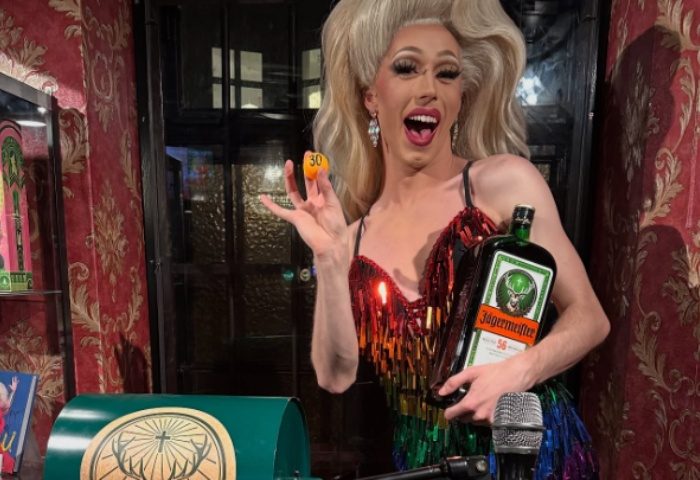 Drag queen at Centre Stage CPH, a gay bar in Copenhagen. She's holding a Jägermeister bottle and a numbered ball, smiling.