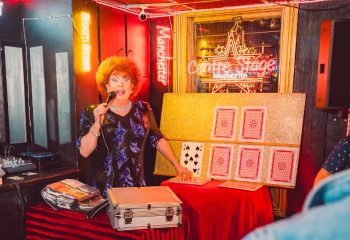 Drag queen at Centre Stage, Manchester, performing a card trick. Neon signs illuminate the gay bar, a popular travel destination. Nightlife.