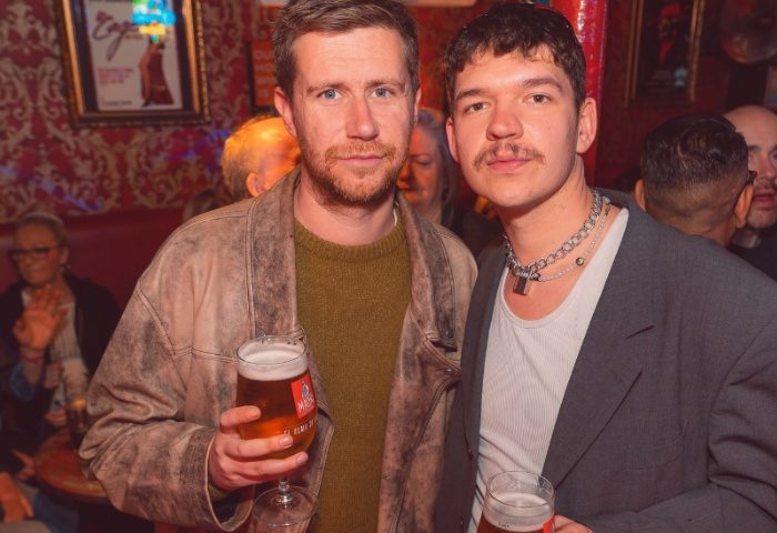 Centre Stage Manchester: Two gay men at a bar, one with a padlock necklace, drinking beer. Gay travel in Manchester, UK.