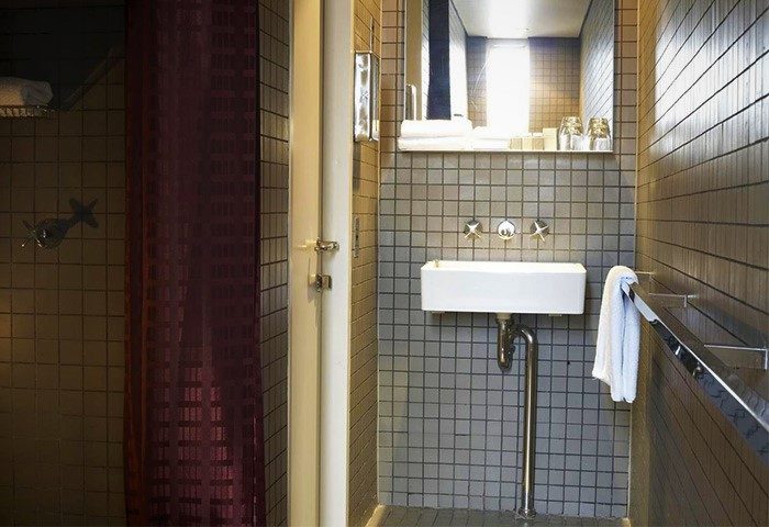 Bathroom in Kirketon Hotel Sydney, a cheap adult-only hotel. Features a shower, white sink, tiled walls, and modern fixtures.