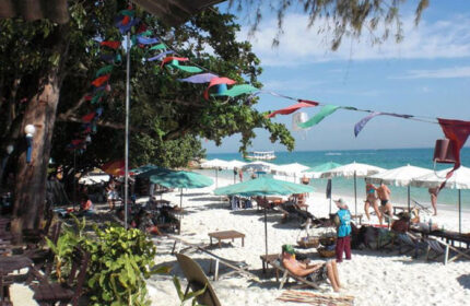 Tok Little Hut: Koh Samet's cheap beachfront gay hotel near gay bars. Sandy beach with umbrellas, sunbathers, and colorful decorations.