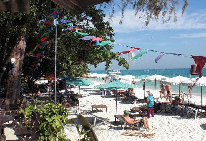 Tok Little Hut: Koh Samet's cheap beachfront gay hotel near gay bars. Sandy beach with umbrellas, sunbathers, and colorful decorations.