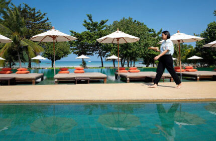 PP Princess Resort beachfront pool view. A server walks by lounge chairs with umbrellas. Cheap gay hotel in Phi Phi Island.