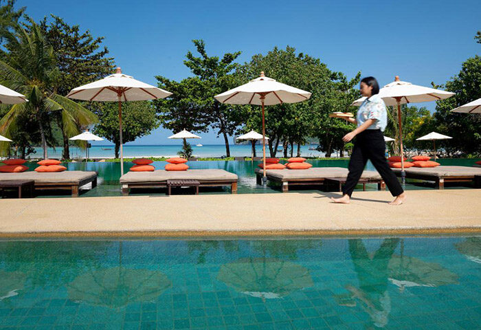 PP Princess Resort beachfront pool view. A server walks by lounge chairs with umbrellas. Cheap gay hotel in Phi Phi Island.