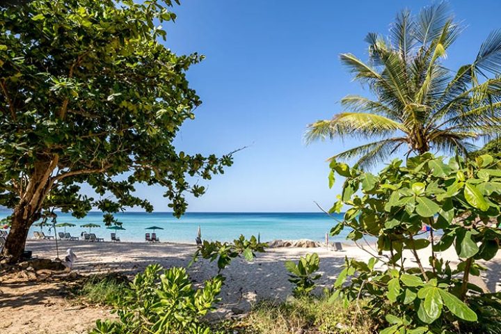 Surin Beach, Thailand. Outrigger Surin Beach Resort beachfront view with palm trees, white sand, and turquoise water. Gay travel Phuket.