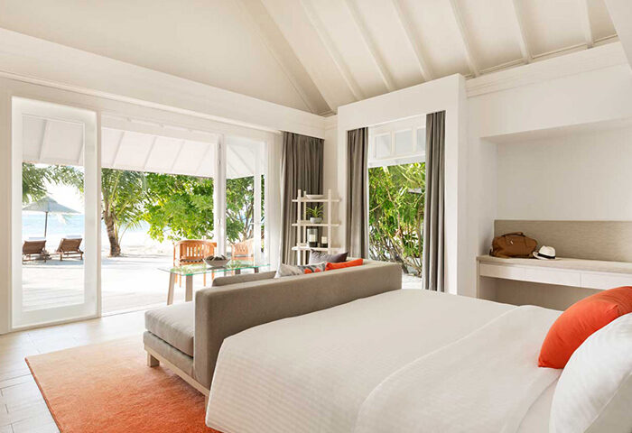 LUX* South Ari Atoll beachfront villa. Maldives gay resort room with beach view, deck chairs, and tropical trees. Cheap gay travel.