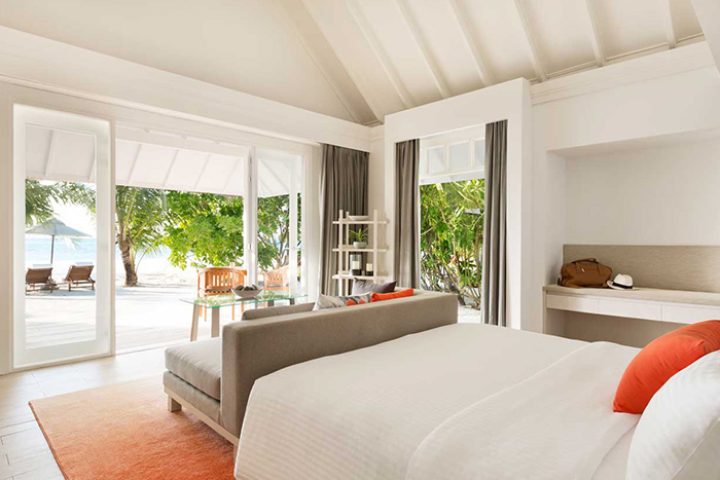 LUX* South Ari Atoll beachfront villa. Maldives gay resort room with beach view, deck chairs, and tropical trees. Cheap gay travel.