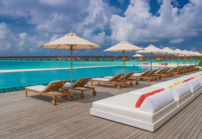 Beachfront pool villas at The Standard, Huruvalhi Maldives, a gay-friendly hotel. Deck chairs and umbrellas line the pool with ocean views.