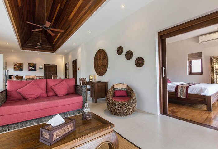 Koh Phangan Pavilions cheap boutique gay hotel room. Living area with red sofa, wooden ceiling, and bedroom view. Tropical decor.