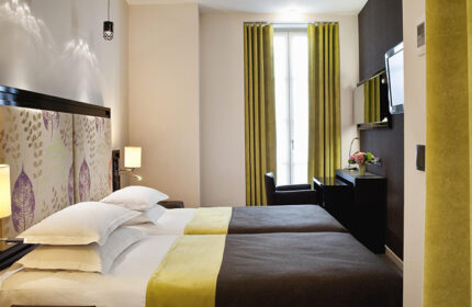 Hotel Caron's comfy room in Paris Marais gayborhood. Twin beds, stylish headboard, desk, and window with green curtains. Cheap & chic gay hotel.