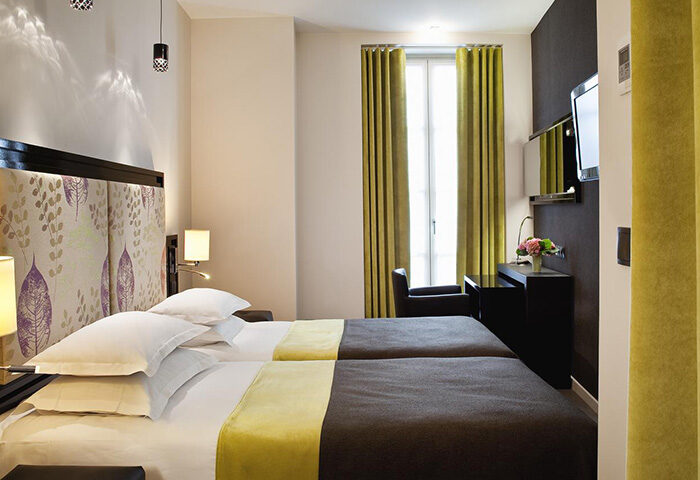 Hotel Caron's comfy room in Paris Marais gayborhood. Twin beds, stylish headboard, desk, and window with green curtains. Cheap & chic gay hotel.