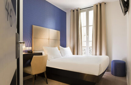 Hotel room at Le Relais du Marais, Paris. Cheap, comfy gay hotel in City Center. Bedroom with double bed, blue accent wall, desk, and window.