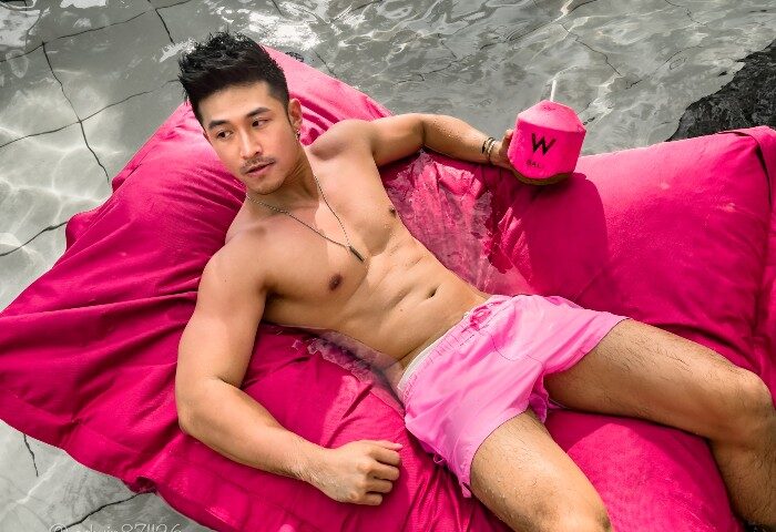 Gay travel: Man relaxing at W Bali Seminyak, a beachfront hotel with a beach club. He's on a pink floatie with a coconut drink.