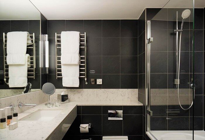 Bathroom at The Nadler Soho, a cheap gay-friendly design hotel in London. Features a shower, sink, towels, and black tile.