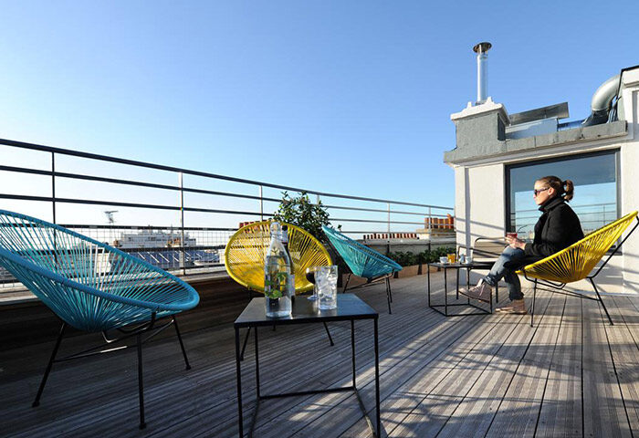 Les Piaules hostel rooftop terrace in Paris. Colorful chairs, tables, and a woman enjoying the view. Gay travel advice.