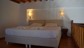 M for Mykonos hotel room. Cheap gay hotel in Mykonos Town near Little Venice. Double bed, wooden floor and ceiling. Gay travel advice.
