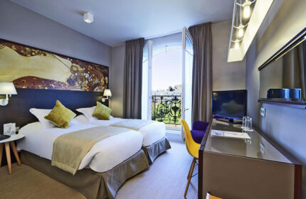 Little Palace Hotel room in Paris' gayborhood. Two twin beds, balcony with view, desk, & Klimt-inspired art. A cheap & chic gay hotel.