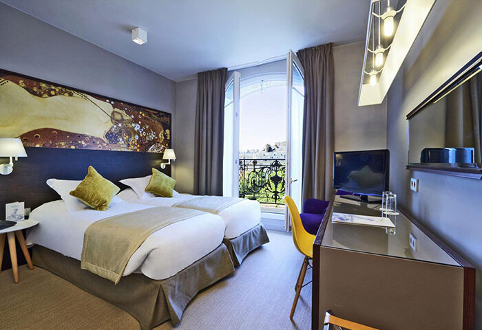 Little Palace Hotel room in Paris' gayborhood. Two twin beds, balcony with view, desk, & Klimt-inspired art. A cheap & chic gay hotel.