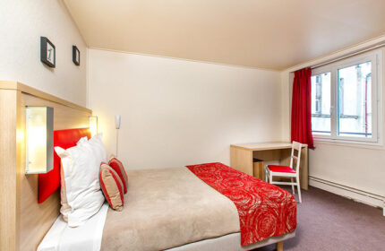 Hotel Dwin, a cheap gay hotel in Paris' Marais gayborhood. Room interior with bed, desk, chair, and window. Gay travel advice.