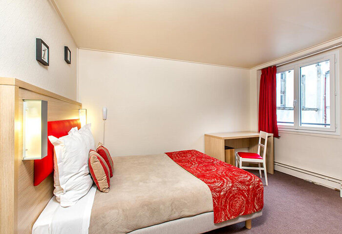 Hotel Dwin, a cheap gay hotel in Paris' Marais gayborhood. Room interior with bed, desk, chair, and window. Gay travel advice.