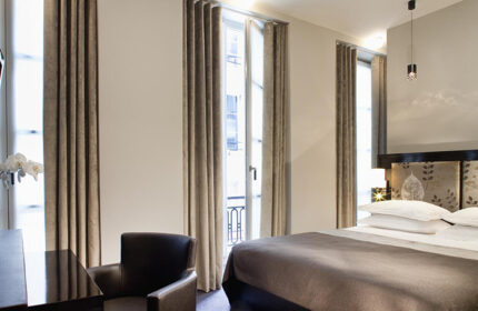 Hotel Caron, a cheap gay hotel in Paris' Marais. Room view with window, bed, and chair. Ideal gay-friendly lodging in Paris.