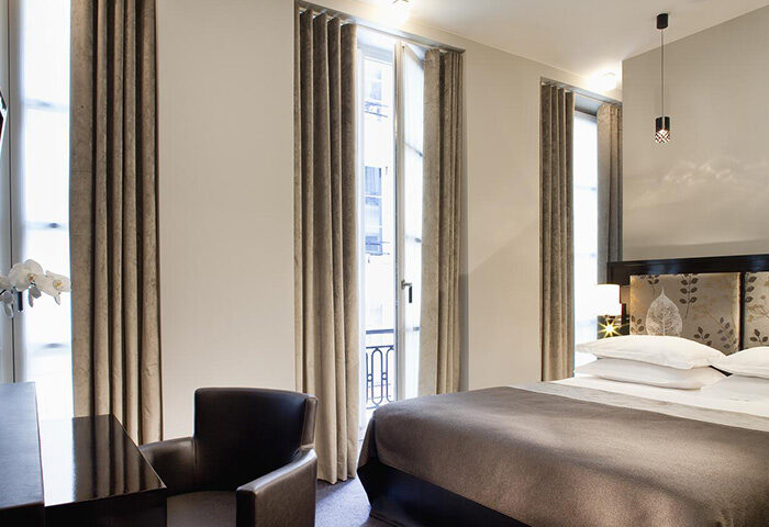 Hotel Caron, a cheap gay hotel in Paris' Marais. Room view with window, bed, and chair. Ideal gay-friendly lodging in Paris.