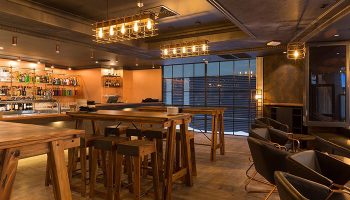 Rydges World Square hotel bar in Sydney's Darlinghurst gayborhood. Rustic wood tables, stools, and caged light fixtures create a warm, inviting space.