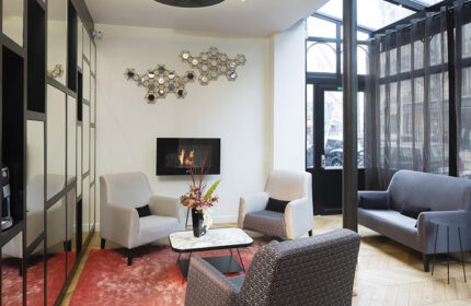 Le Relais du Marais Hotel lobby, a cheap gay hotel in Paris. Cozy seating area with a fireplace, armchairs, and sofa. Stylish design.