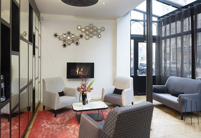 Le Relais du Marais Hotel lobby, a cheap gay hotel in Paris. Cozy seating area with a fireplace, armchairs, and sofa. Stylish design.