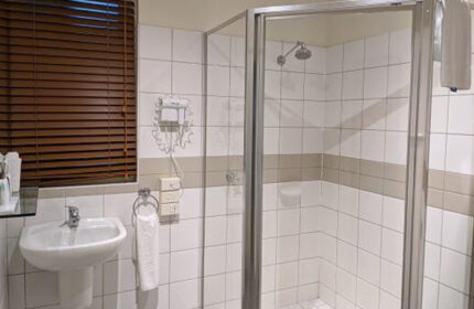 Bathroom at Tolarno Hotel, a cheap gay hotel in Melbourne's gayborhood, St Kilda. Sink, shower, and brown blinds visible.